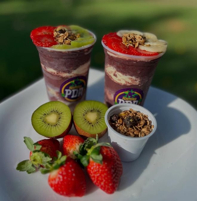 Dois copos de açaí com morango, kiwi, banana e granola, servidos com frutas frescas ao lado